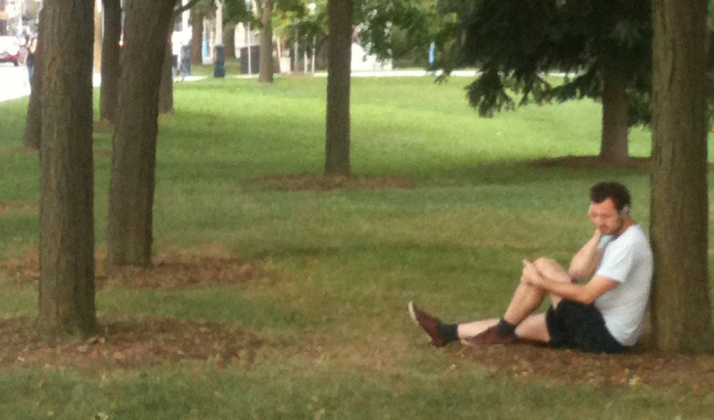 A man is sitting under a tree listening to something on headphones.