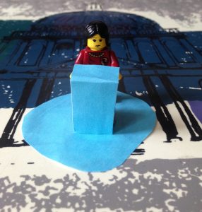 A lego figure with a concerned expression is standing against a blue podium